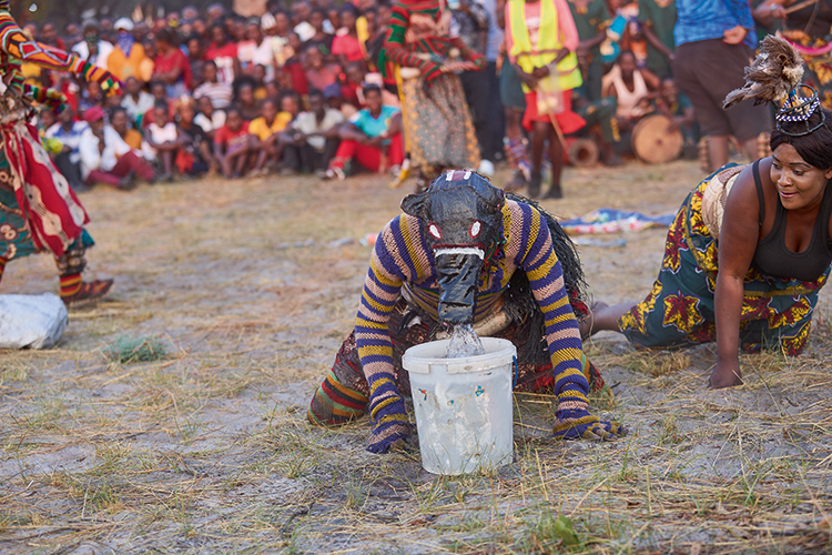 Likishi Ngulu (pig spirit) exhibits a pig’s behaviour by playing in stagnant water and unkempt environments. His role is to entertain spectators. (Image by Nkwazi/Justine Kunda).